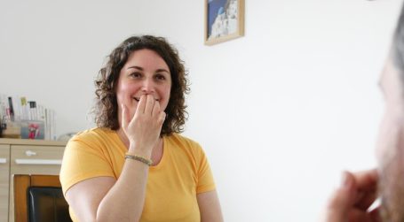 Femme souriante en t-shirt jaune, mains sur le visage, dans un cadre intérieur.
