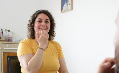 Femme souriante en t-shirt jaune en train de discuter avec une autre personne.